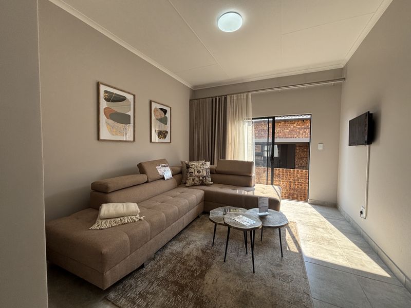 A well-maintained living room featuring neutral wall tones, tiled flooring, and a sliding glass door providing access to the exterior.