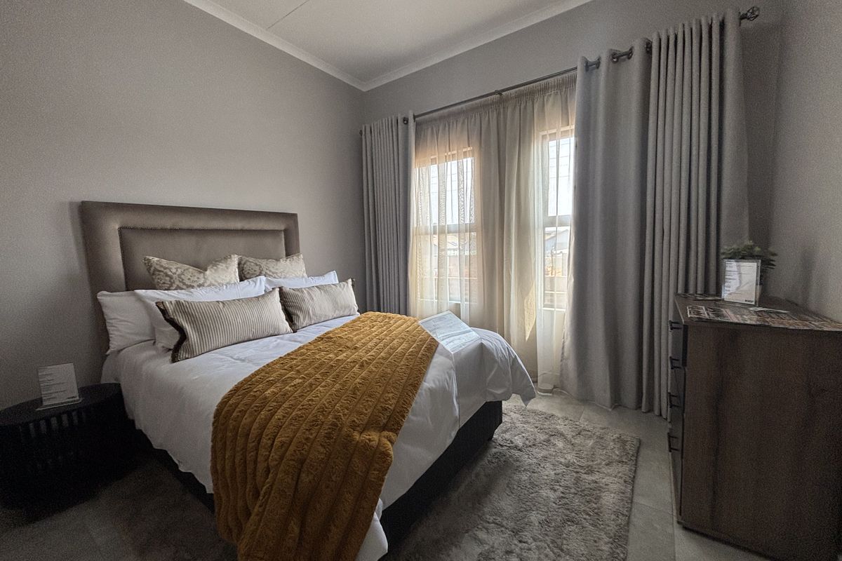 A well-maintained bedroom featuring neutral wall tones, tiled flooring, and large windows dressed with floor-to-ceiling curtains.