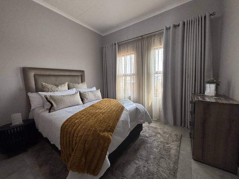 A well-maintained bedroom featuring neutral wall tones, tiled flooring, and large windows dressed with floor-to-ceiling curtains.