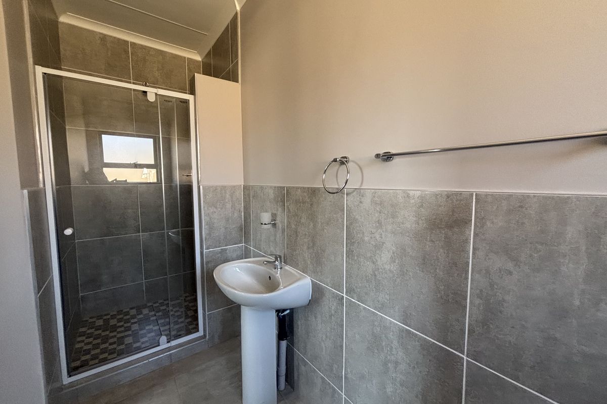 A clean, modern bathroom featuring a pedestal basin, a glass-enclosed shower, and neutral grey wall and floor tiling.