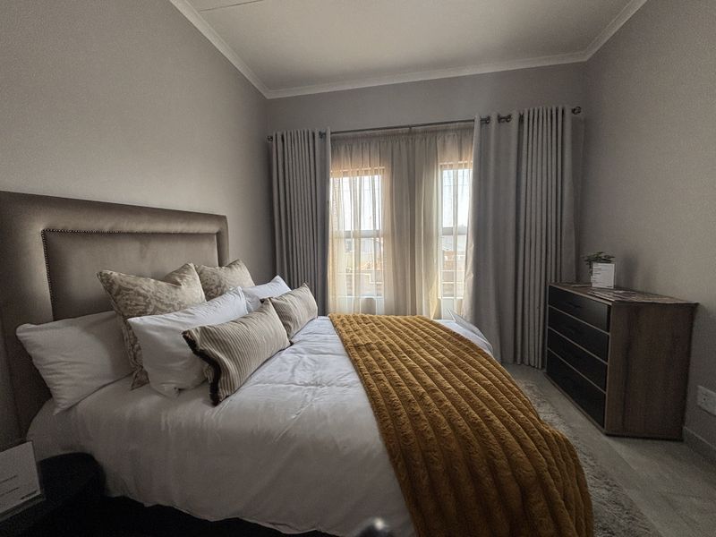 A well-maintained bedroom featuring neutral wall tones, laminate flooring, and floor-to-ceiling curtain treatments.