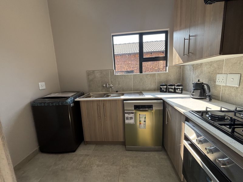 A modern kitchen featuring wood-finish cabinetry, stone countertops, a gas hob, built-in oven, and a double sink with tiled backsplash.