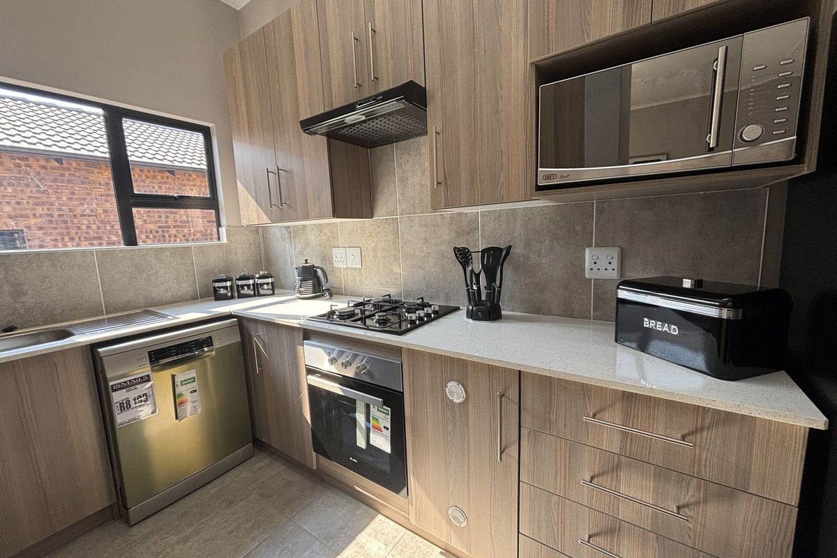 Modern kitchen featuring wood-finish cabinetry, stone countertops, built-in gas hob, oven, extractor fan, and integrated appliances with a tiled backsplash.