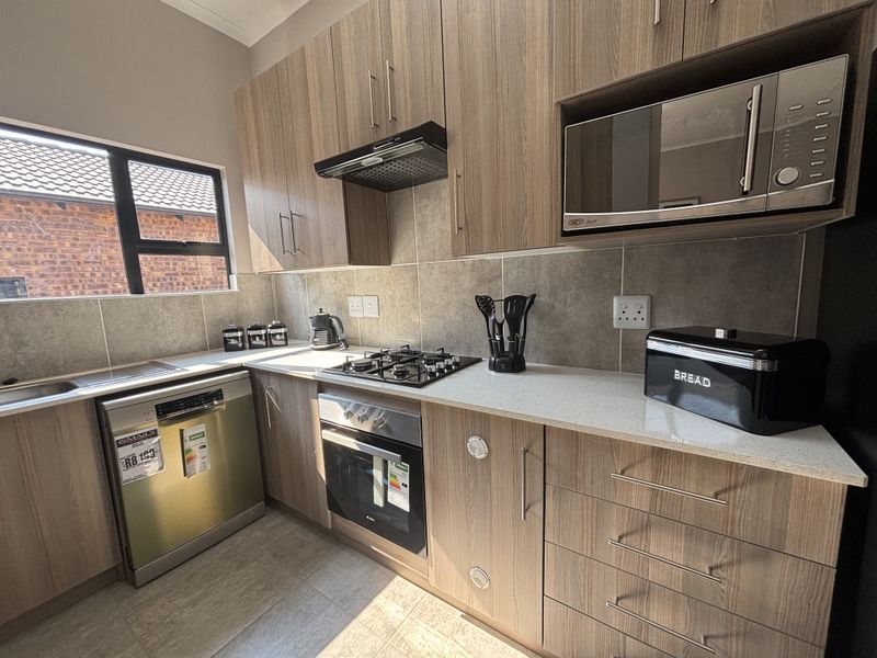Modern kitchen featuring wood-finish cabinetry, stone countertops, built-in gas hob, oven, extractor fan, and integrated appliances with a tiled backsplash.