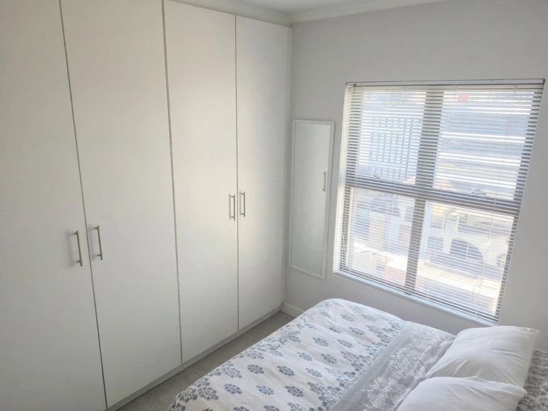 A bright bedroom featuring floor-to-ceiling built-in cupboards and a window fitted with venetian blinds.