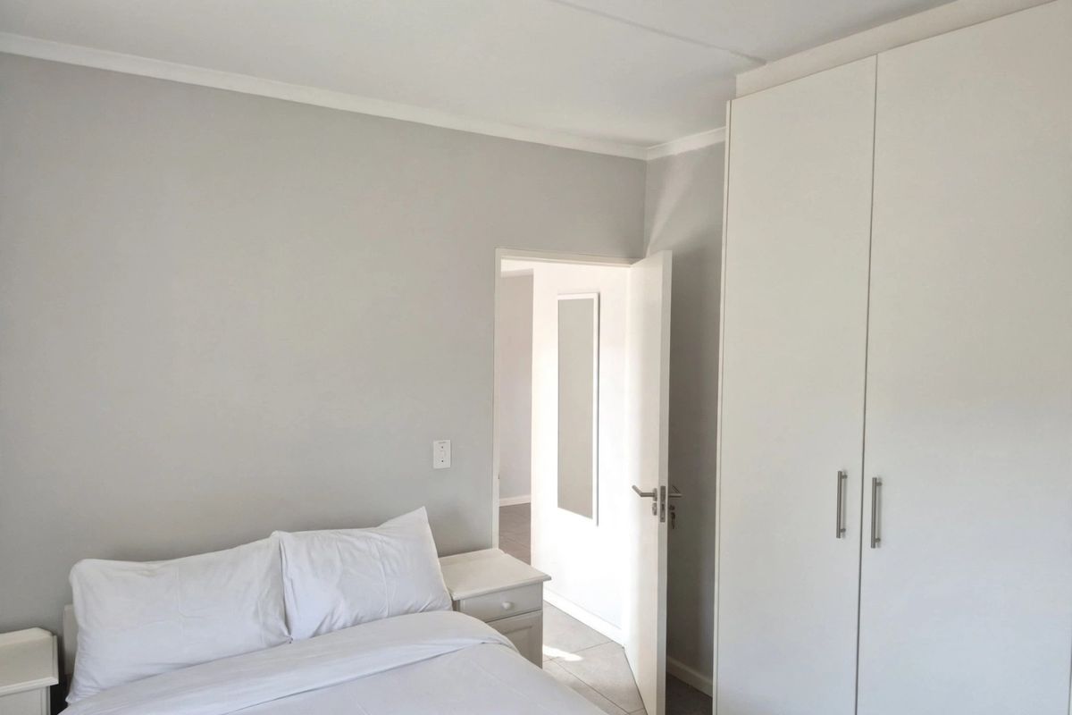 A clean and bright bedroom featuring neutral wall tones, tiled flooring, and a spacious white built-in wardrobe.