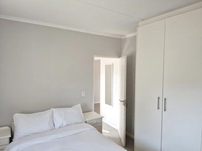A clean and bright bedroom featuring neutral wall tones, tiled flooring, and a spacious white built-in wardrobe.
