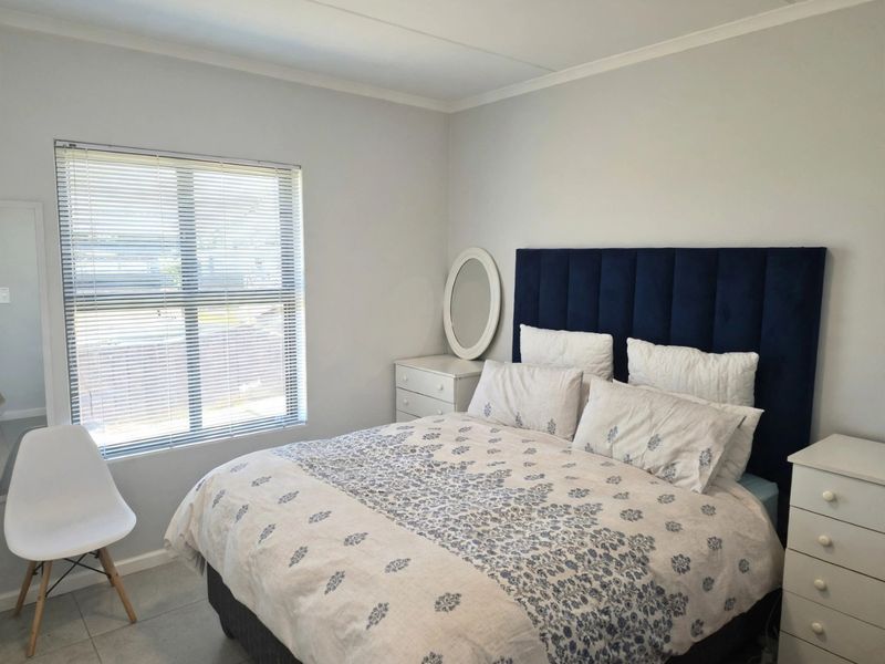 A well-maintained bedroom featuring neutral wall tones, tiled flooring, and a large window fitted with venetian blinds.