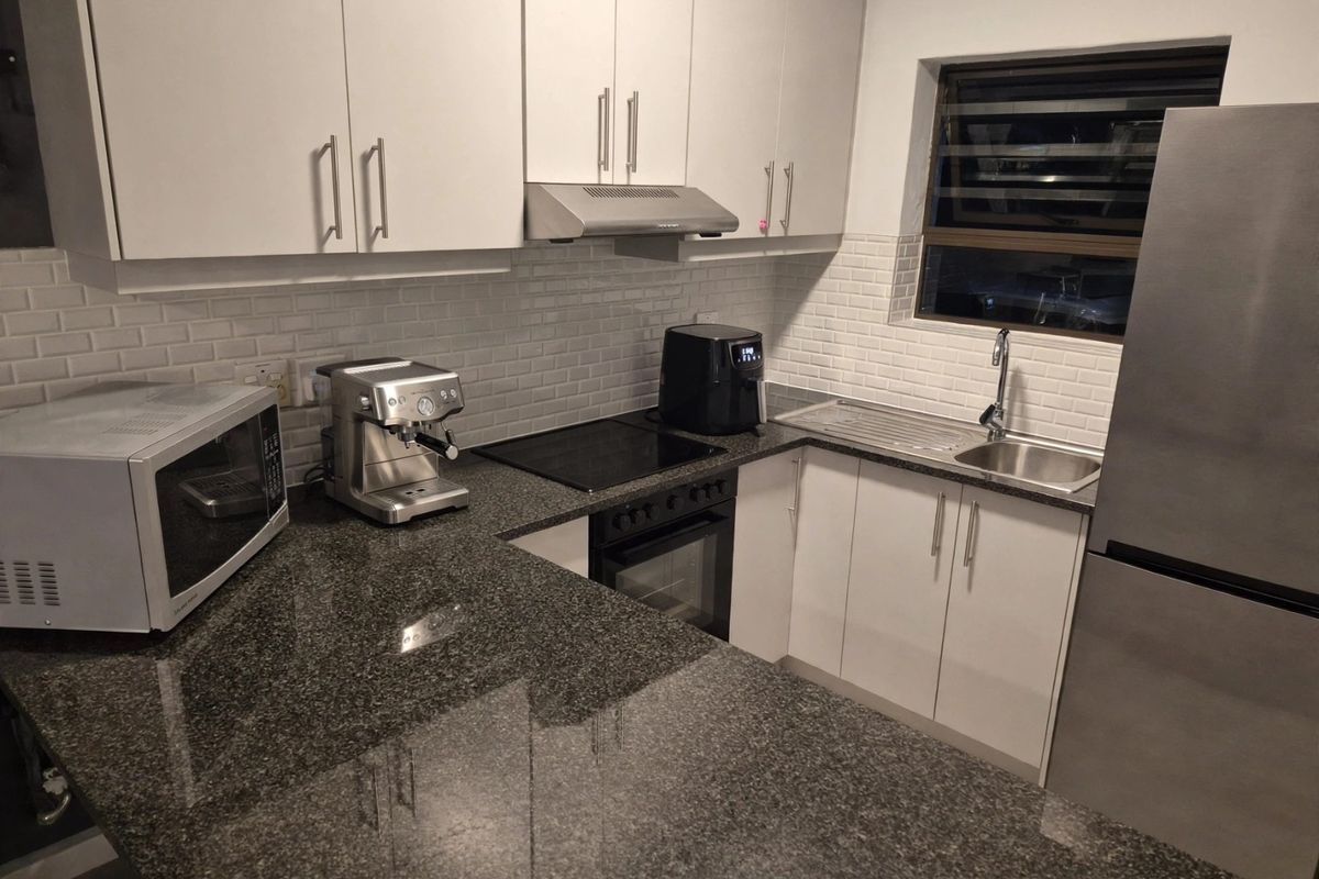 Modern kitchen featuring white cabinetry, granite countertops, subway tile backsplash, and integrated appliances including an oven, hob, and extractor fan.