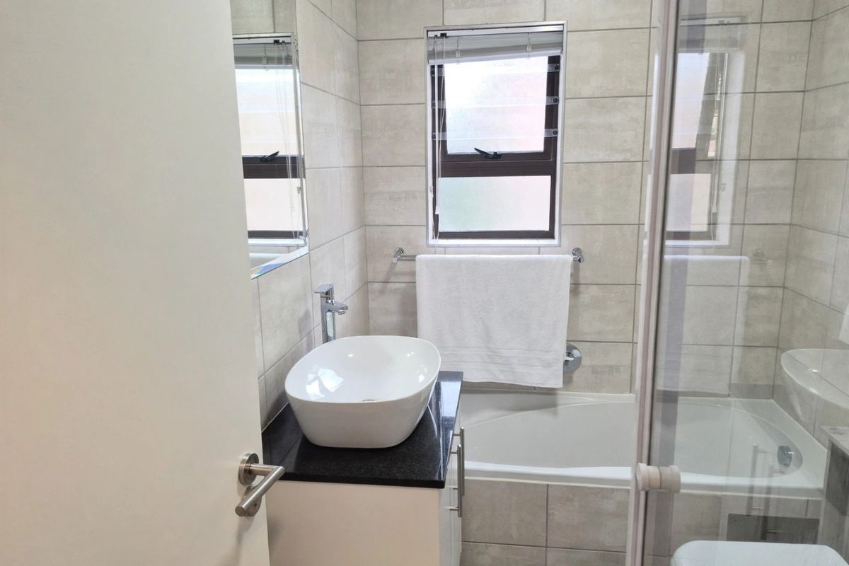 Modern bathroom featuring a vessel sink on a granite vanity, a bathtub with a glass shower enclosure, and neutral wall tiling.