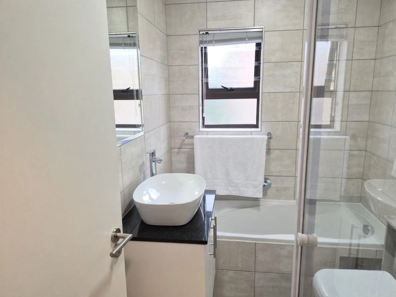 Modern bathroom featuring a vessel sink on a granite vanity, a bathtub with a glass shower enclosure, and neutral wall tiling.