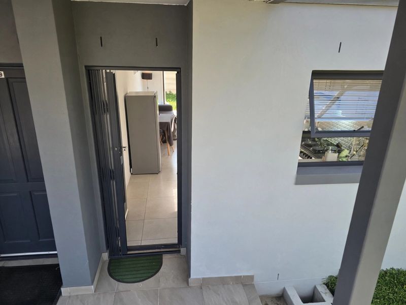 An exterior view of the apartment entrance featuring a modern folding door, tiled threshold, and a top-hung window looking into the kitchen area.