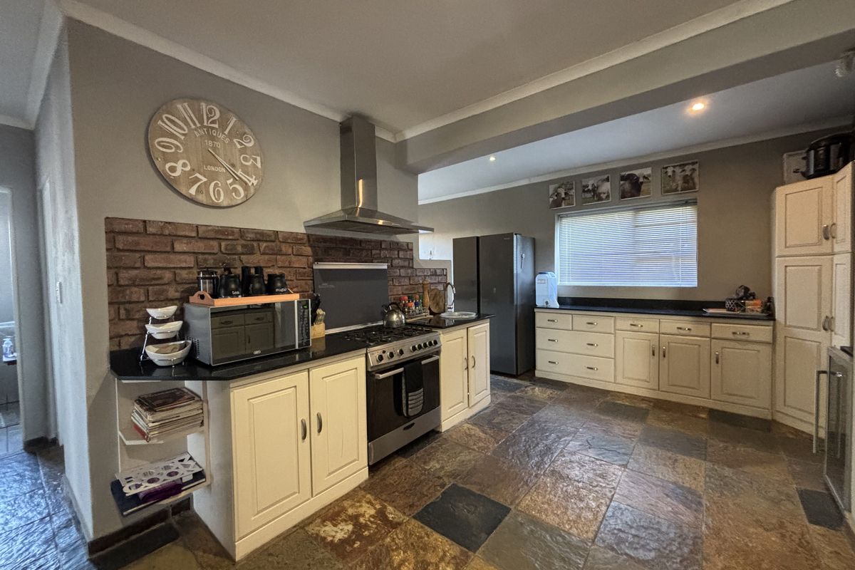 Spacious kitchen featuring a brick feature wall, stainless steel extractor fan, gas stove, dark granite countertops, and slate tile flooring.