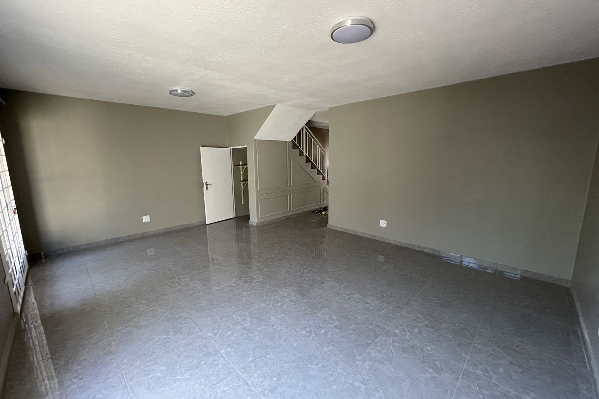Spacious, empty living area featuring neutral wall tones, large format floor tiles, and a staircase with integrated under-stair storage.