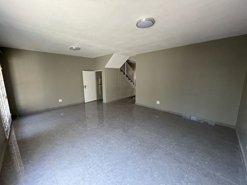 Spacious, empty living area featuring neutral wall tones, large format floor tiles, and a staircase with integrated under-stair storage.
