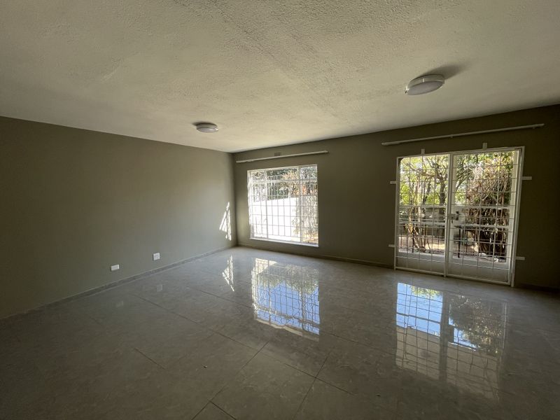 Spacious, empty living area featuring polished tile flooring, neutral wall tones, and secure access to the exterior via sliding glass doors with security gates.