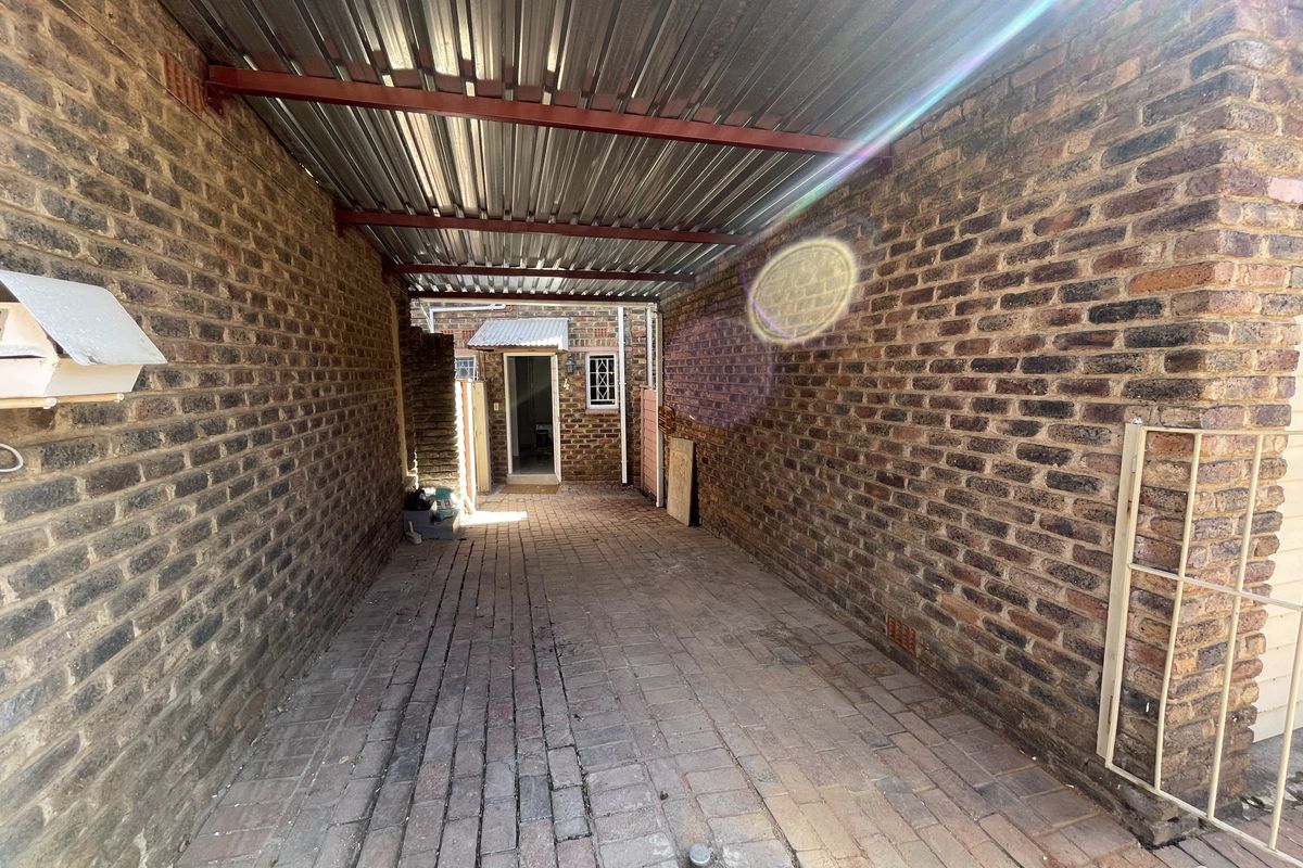 A covered outdoor walkway or utility area featuring exposed brick walls, corrugated metal roofing, and brick paving.