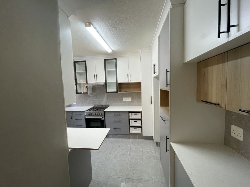 A modern, well-lit kitchen featuring two-tone cabinetry, stone countertops, a gas stove with extractor fan, and neutral tiled flooring.