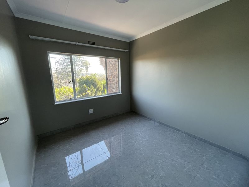 A bright, empty bedroom featuring neutral wall paint, modern tiled flooring, and a window fitted with security bars and a curtain rail.