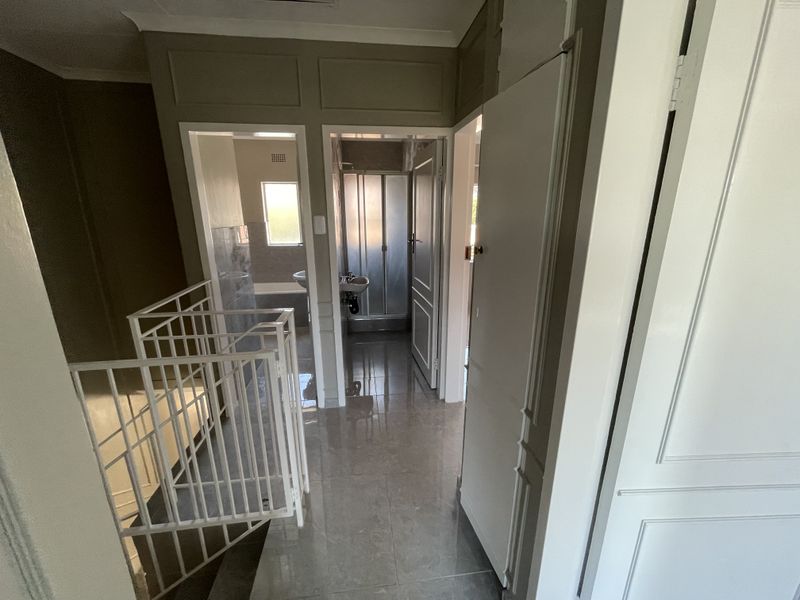 A bright upper-level hallway featuring tiled flooring, decorative wall panelling, and a metal balustrade, providing access to adjacent bathroom facilities.