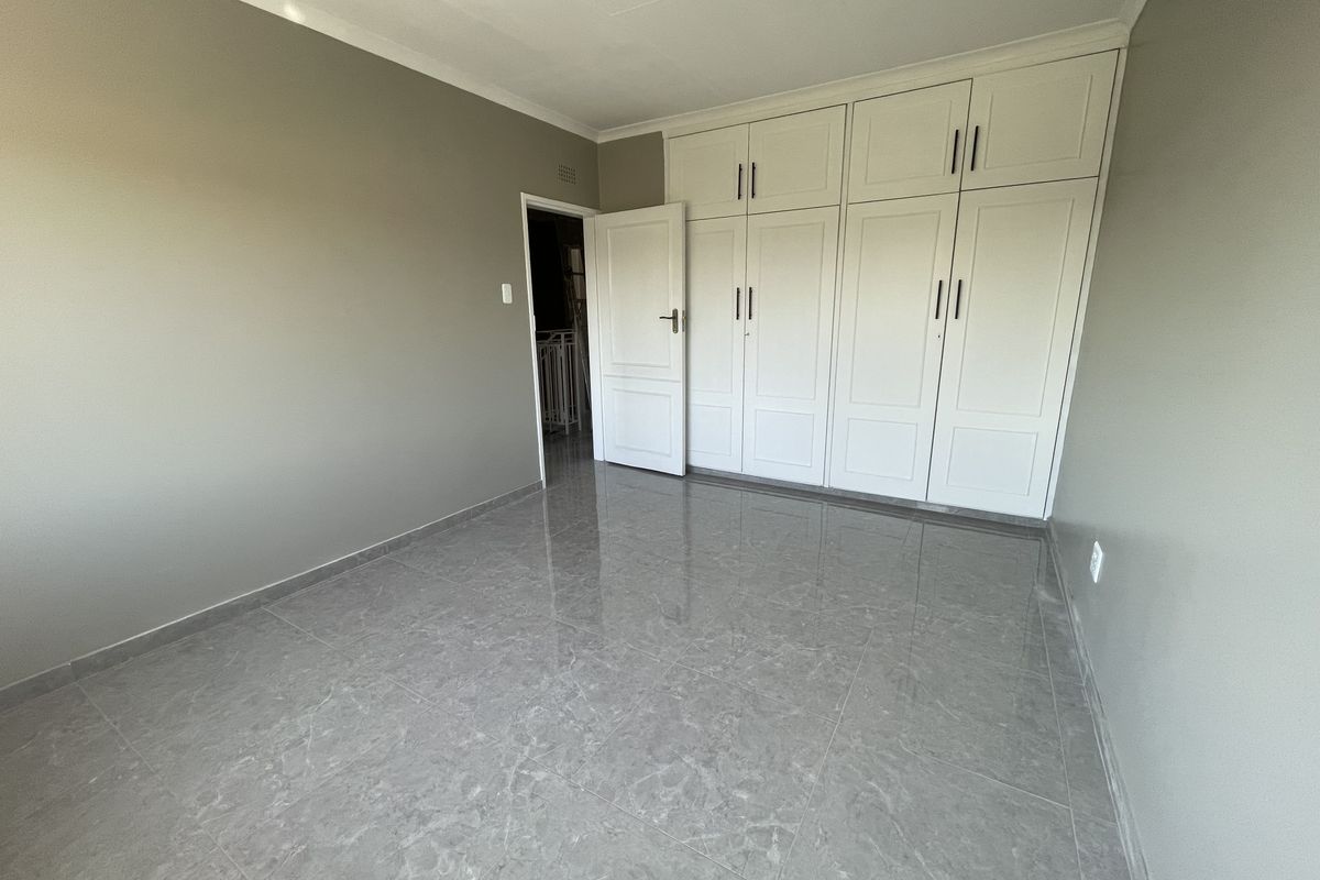 A clean, empty bedroom featuring modern grey tiled flooring, neutral wall paint, and extensive white built-in cabinetry with overhead storage.