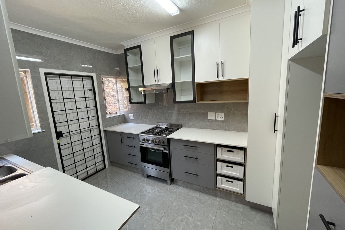 Modern kitchen featuring sleek two-tone cabinetry, stone countertops, a gas stove with extractor fan, and tiled flooring with direct access to a security gate.