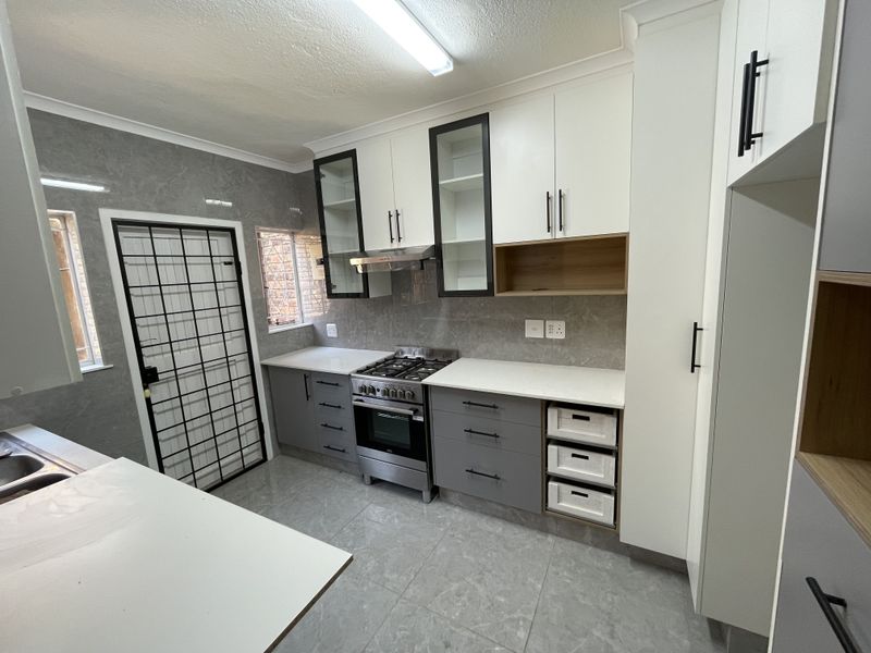 Modern kitchen featuring sleek two-tone cabinetry, stone countertops, a gas stove with extractor fan, and tiled flooring with direct access to a security gate.
