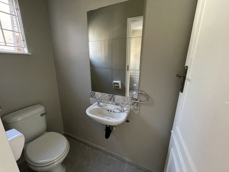 A compact guest bathroom featuring a wall-mounted basin with a tiled splashback, a wall mirror, and a standard toilet.