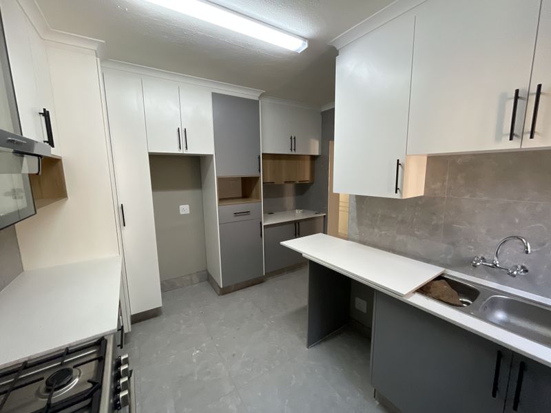 Modern kitchen featuring two-tone cabinetry, stone countertops, gas hob, extractor fan, and a double bowl sink with tiled finishes.