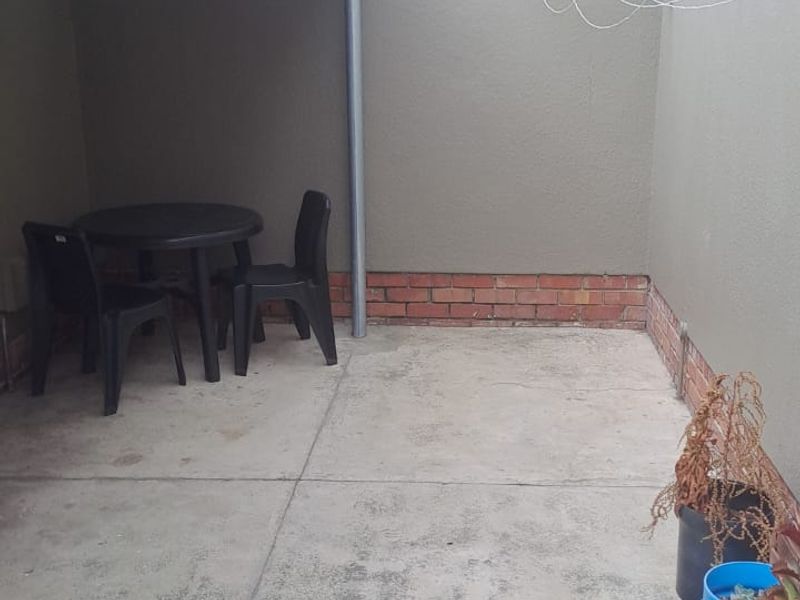 A covered outdoor patio area featuring concrete flooring, a brick baseboard, and a wall-mounted clothesline.