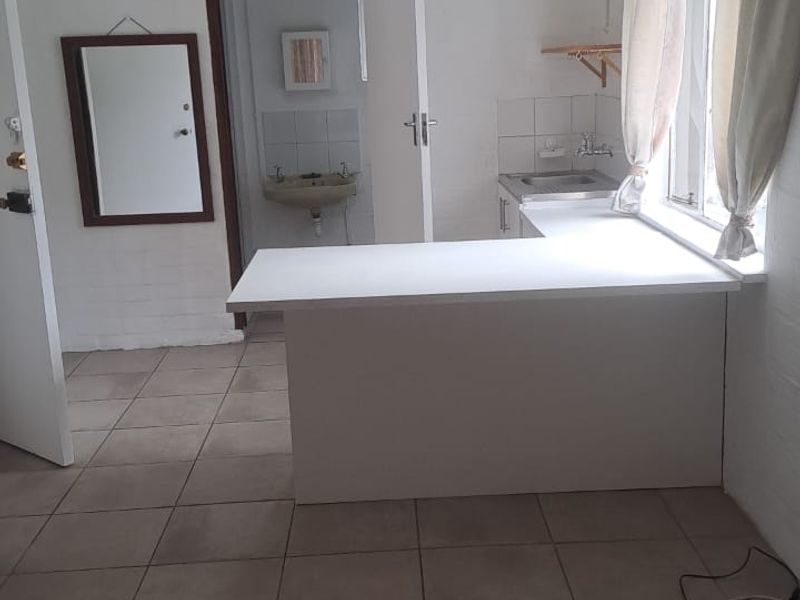 A compact kitchen area featuring a built-in counter, sink, and tiled flooring, offering a functional space ready for modernization.