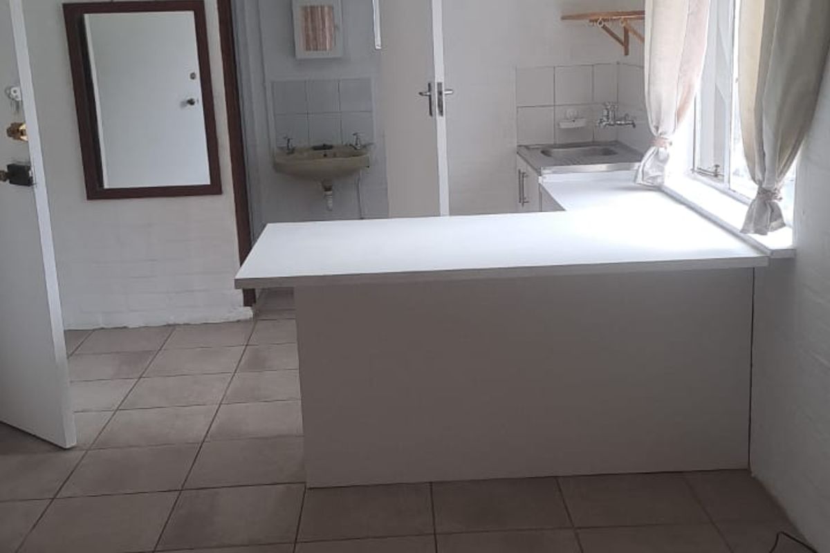 A compact kitchen area featuring a built-in counter, sink, and tiled flooring, offering a functional space ready for modernization.