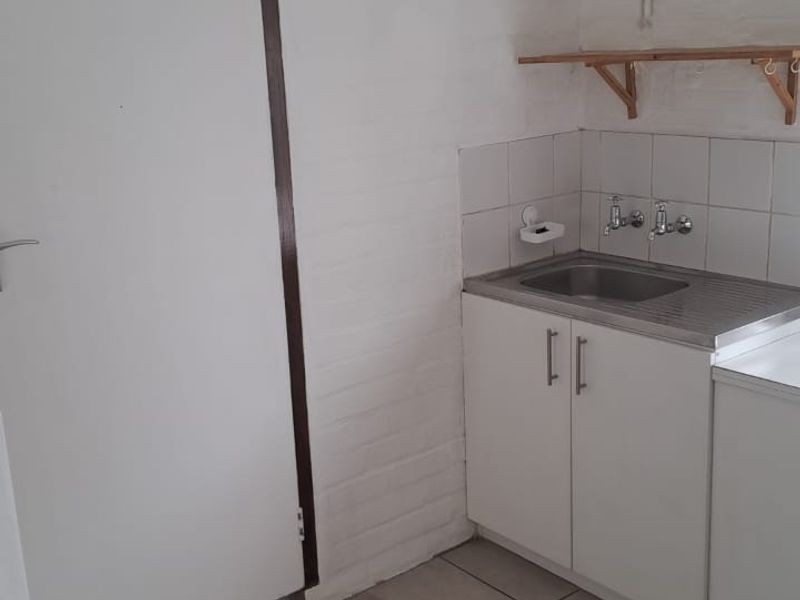 A functional scullery or utility area featuring a stainless steel sink, tiled splashback, built-in base cabinetry, and wall-mounted shelving.