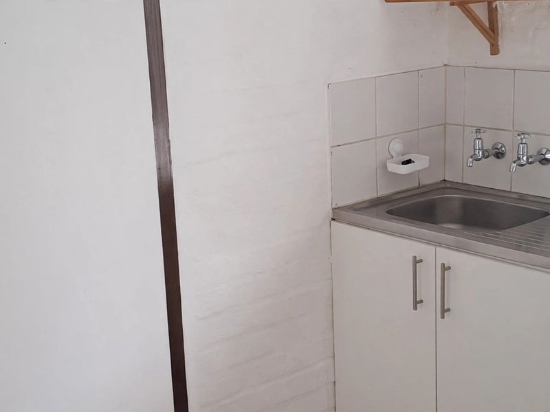A compact kitchen area featuring a stainless steel sink, tiled splashback, and basic built-in cabinetry with wall-mounted shelving.