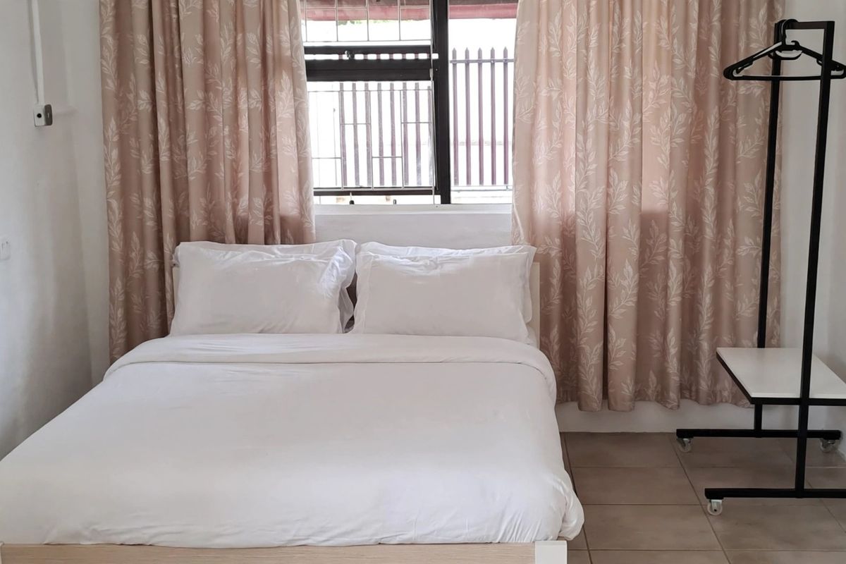 A functional bedroom featuring tiled flooring and a window fitted with security bars, providing a simple and practical living space.