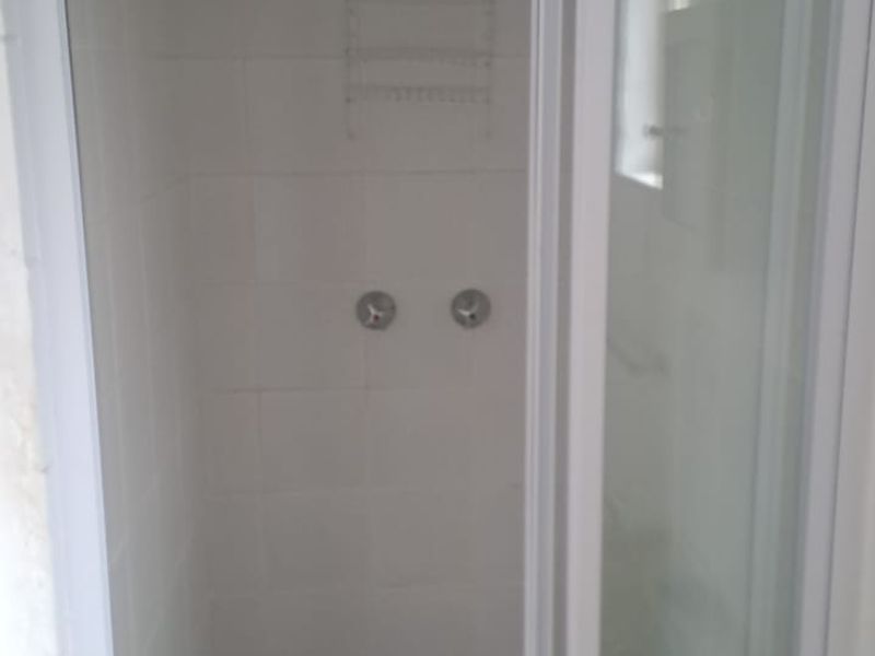 A functional bathroom shower enclosure with white tiled walls and a separate basin area.