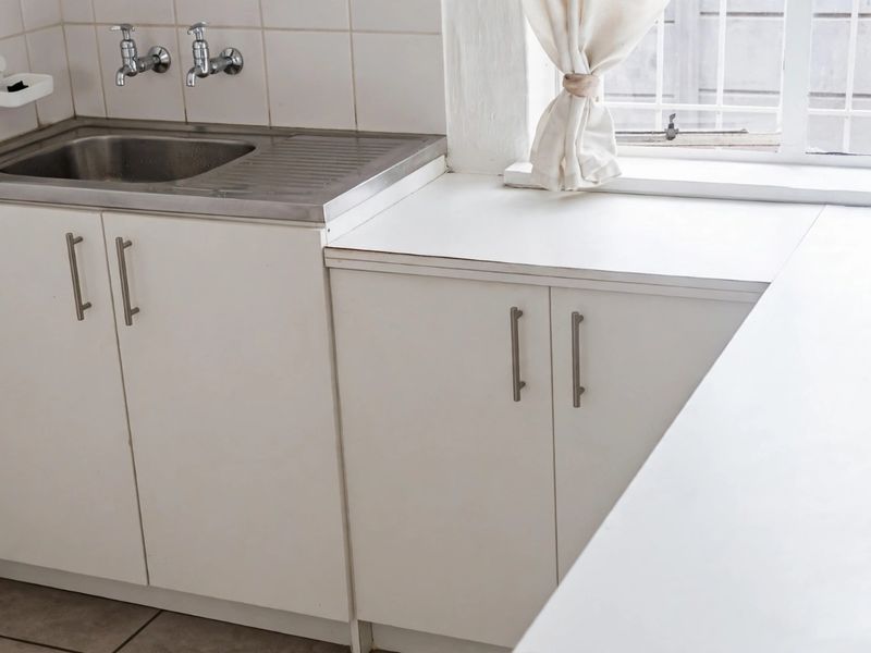 A functional kitchen area featuring built-in white cabinetry, a stainless steel sink, and tiled splashbacks, offering a clean and practical workspace.