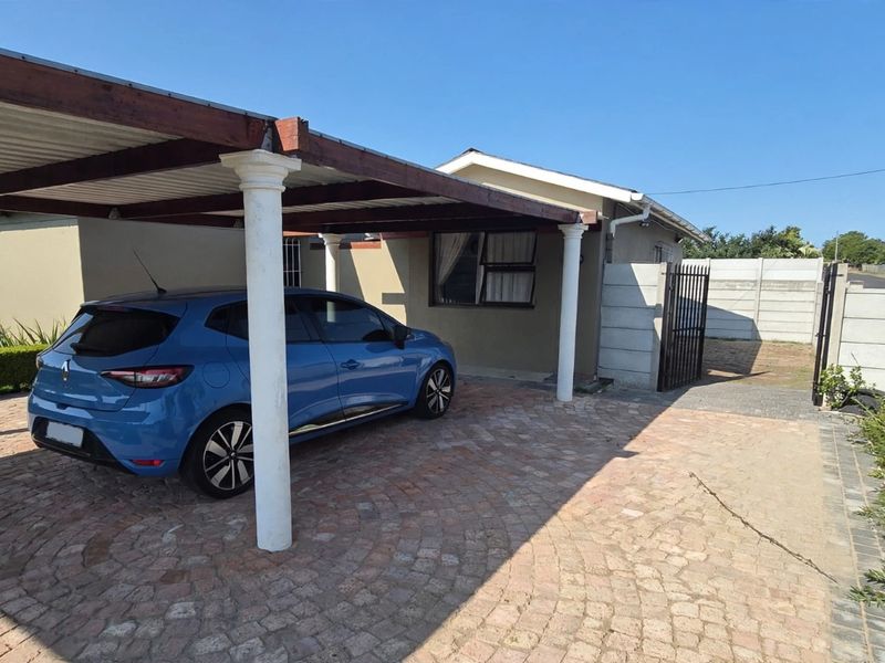 Front exterior view of the property featuring a paved driveway, a covered carport, and secure boundary walling.