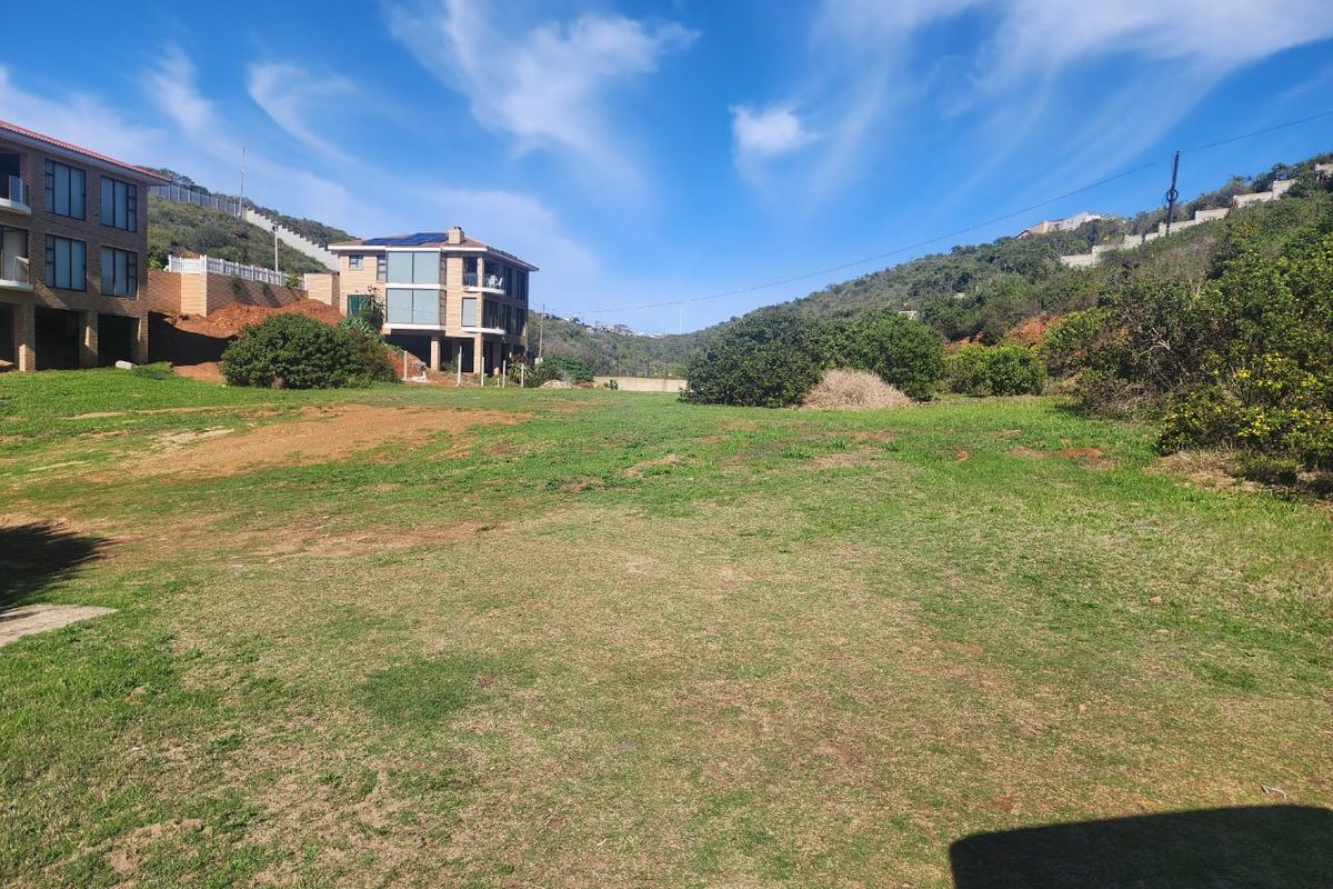 A view of a vacant residential plot featuring sloped grassy terrain with surrounding hillside landscape and neighboring residential properties.