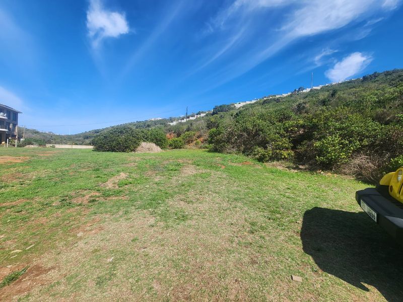 A view of a sloped, grassy residential plot with natural vegetation and surrounding hillside landscape.