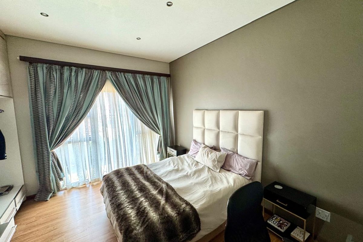 A well-maintained bedroom featuring laminate flooring, recessed ceiling lighting, and a large window with floor-to-ceiling curtains providing natural light.