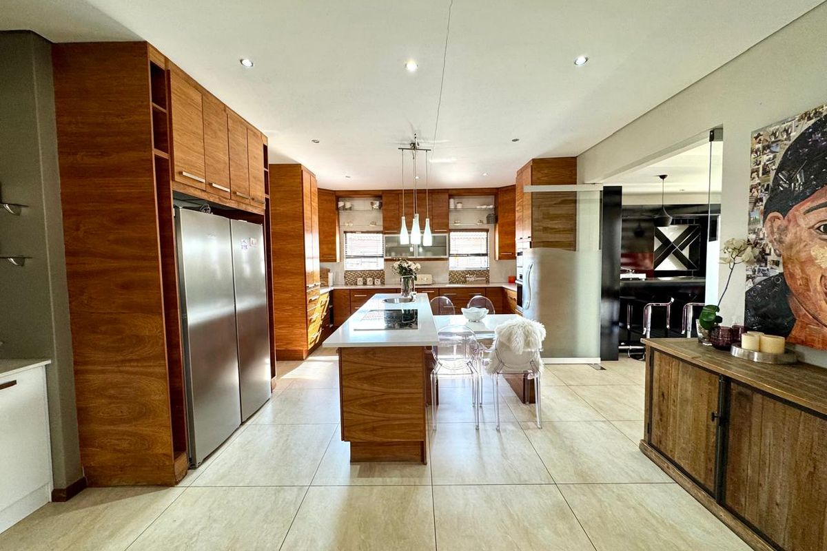 Modern kitchen featuring warm wood cabinetry, a central island with integrated cooktop, stone countertops, and large format floor tiles.