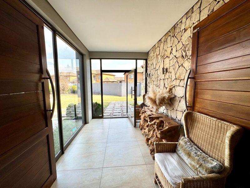 A bright and welcoming entrance hall featuring large glass doors, tiled flooring, and a striking natural stone feature wall.