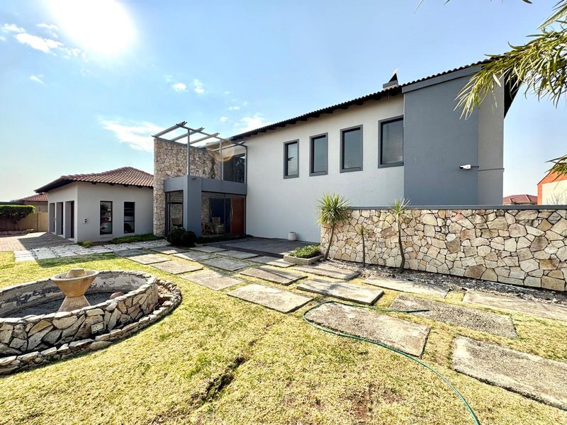 Rear view of the property featuring a landscaped garden, stone-clad feature wall, paved walkway, and a decorative stone fountain.