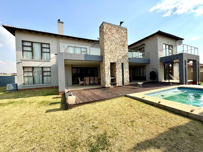 Rear view of a double-story residence featuring a stone-clad chimney, wooden decking, a swimming pool, and upper-level balconies with glass balustrades.