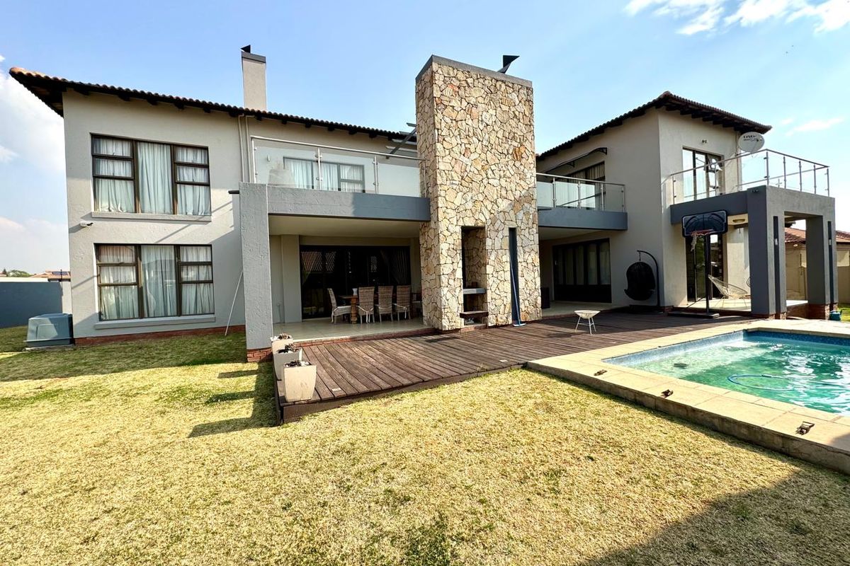 Rear view of a double-story residence featuring a stone-clad chimney, wooden decking, a swimming pool, and upper-level balconies with glass balustrades.
