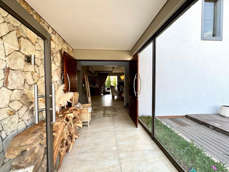 A bright, modern entrance hall featuring natural stone cladding, large format floor tiles, and expansive glass panels opening onto a timber deck.