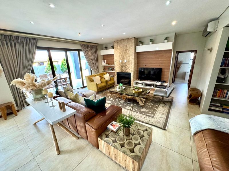 Spacious open-plan living area featuring a stone-clad fireplace, large sliding glass doors leading to the patio, and modern tiled flooring.