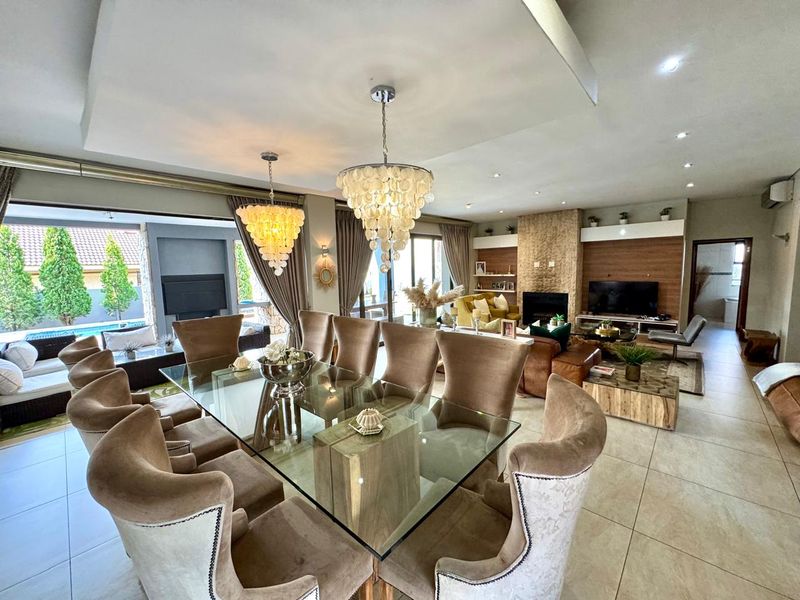 Spacious open-plan living and dining area featuring a stone-clad fireplace, recessed ceiling lighting, and seamless flow to the outdoor patio and pool area.
