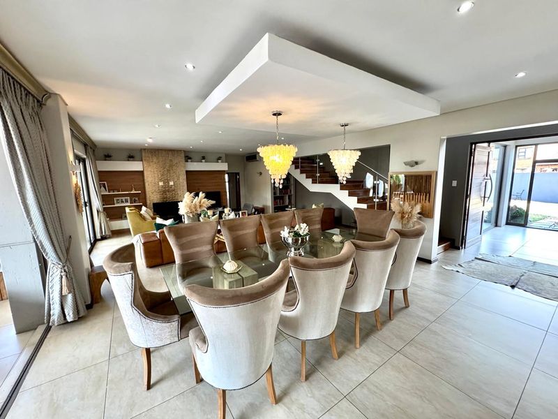 Spacious open-plan dining and living area featuring large format floor tiles, a dropped ceiling detail with pendant lighting, and a modern staircase.